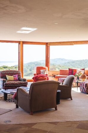 A spacious living room with large windows, a sofa, armchairs, and a coffee table.
