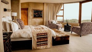 A bedroom with a large bed, a chair, a side table, and a view of the landscape. - Sandcastle (Wesley)