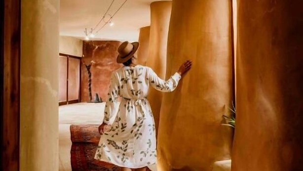A corridor with large cylindrical columns, a person in a dress, and a carpeted floor.