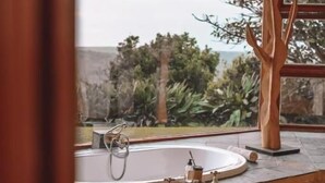 A bathroom with a bathtub, a window, and a view of trees and a building. - Sandcastle (Wesley)