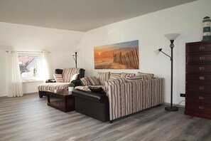 A living room with a sofa, armchair, and coffee table, a painting on the wall, and a lamp. - Holiday apartment with 2 bedrooms (Carolinensiel)