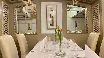 A dining area with a long table set for a meal, surrounded by chairs, with star-shaped decorations on the ceiling and a framed artwork on the wall.