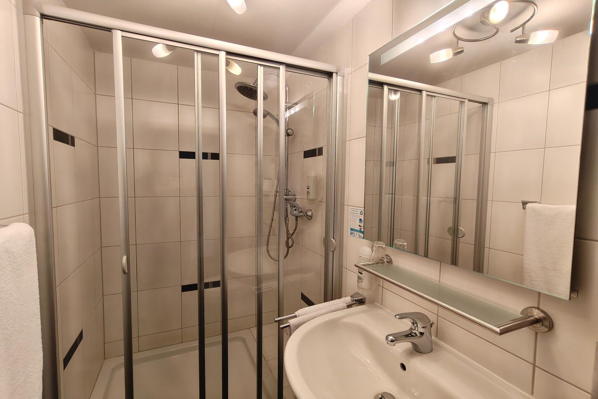 Un bany modern amb dutxa de vidre, un lavabo amb mirall i una barra de tovalloles.