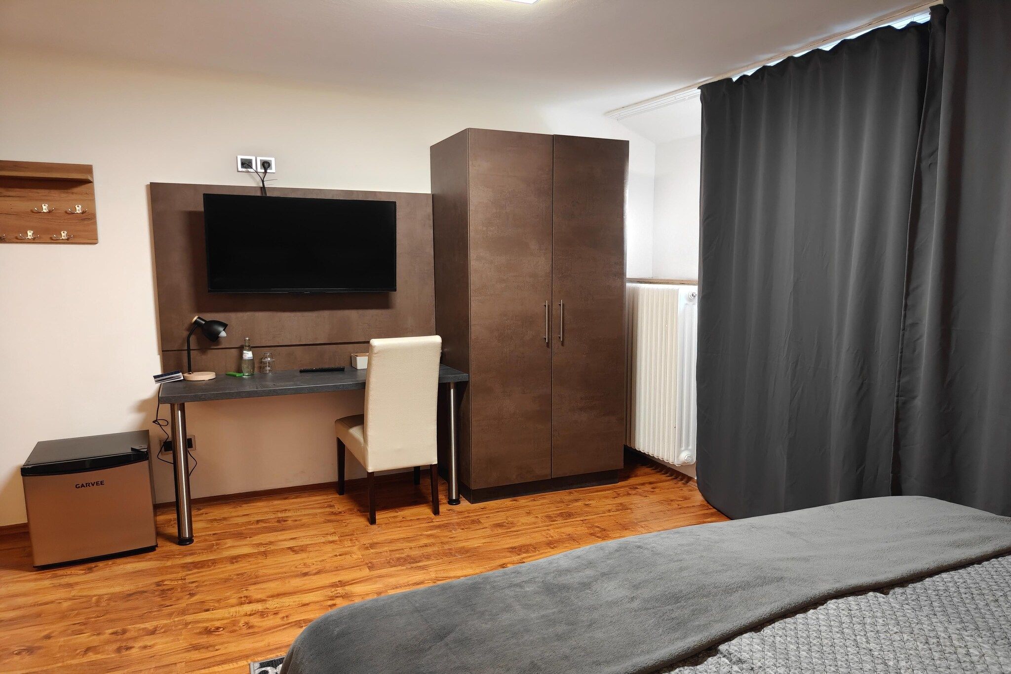 Ein Hotelzimmer mit einem Bett, einem Schreibtisch mit Stuhl, einem Kleiderschrank, einem Fernseher und einer Heizung.