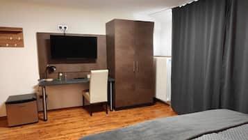 A hotel room with a bed, a desk with a chair, a wardrobe, a television, and a radiator.
