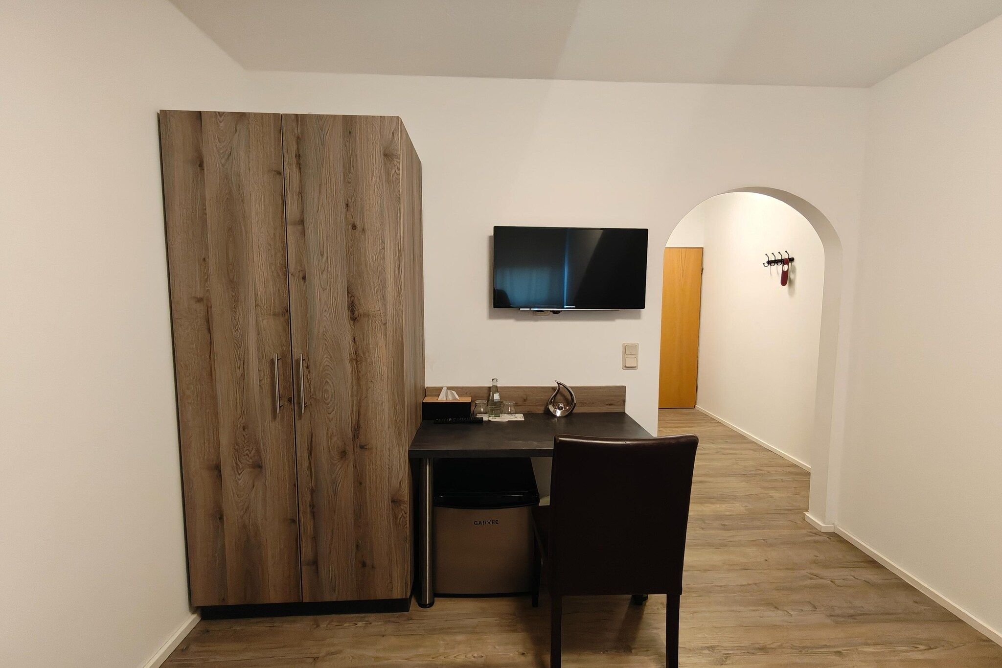 Eine kompakte Küche mit einem Holzkorpus, einem Esstisch, einem Stuhl und einem an der Wand befestigten Flachbildfernseher.