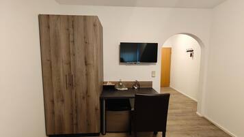 Eine kompakte Küche mit einem Holzkorpus, einem Esstisch, einem Stuhl und einem an der Wand befestigten Flachbildfernseher.