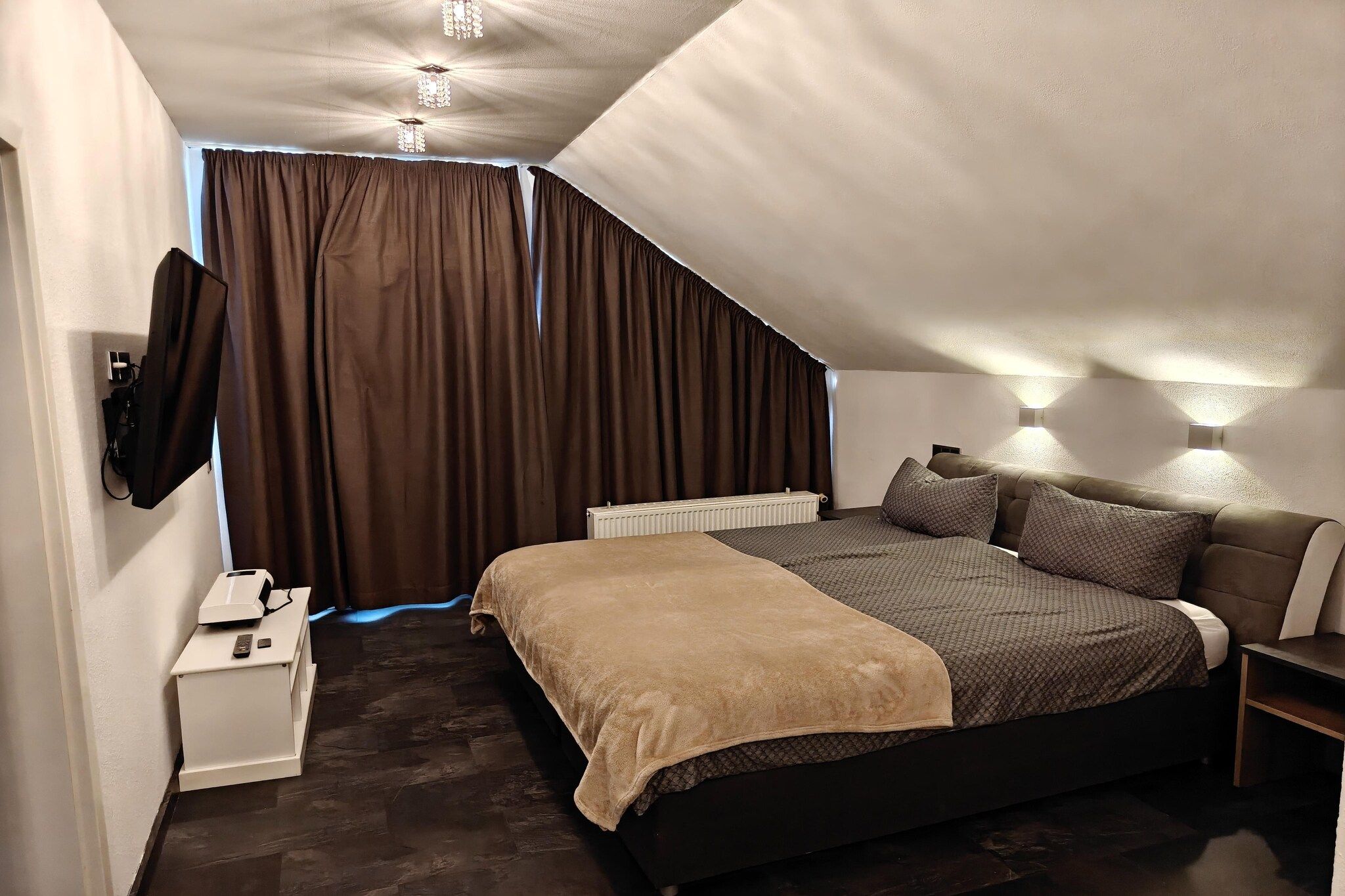 Een slaapkamer met een bed, nachtkastjes, een radiator en een aan de muur bevestigde televisie.