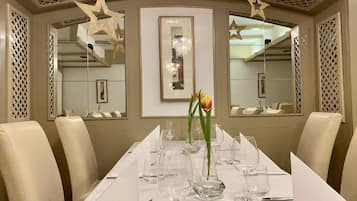A dining area with a long table set for a meal, surrounded by chairs, with star-shaped decorations on the ceiling and a framed artwork on the wall.