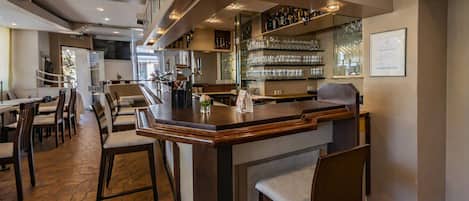 A bar area with a counter, chairs, and shelves of glasses and bottles.