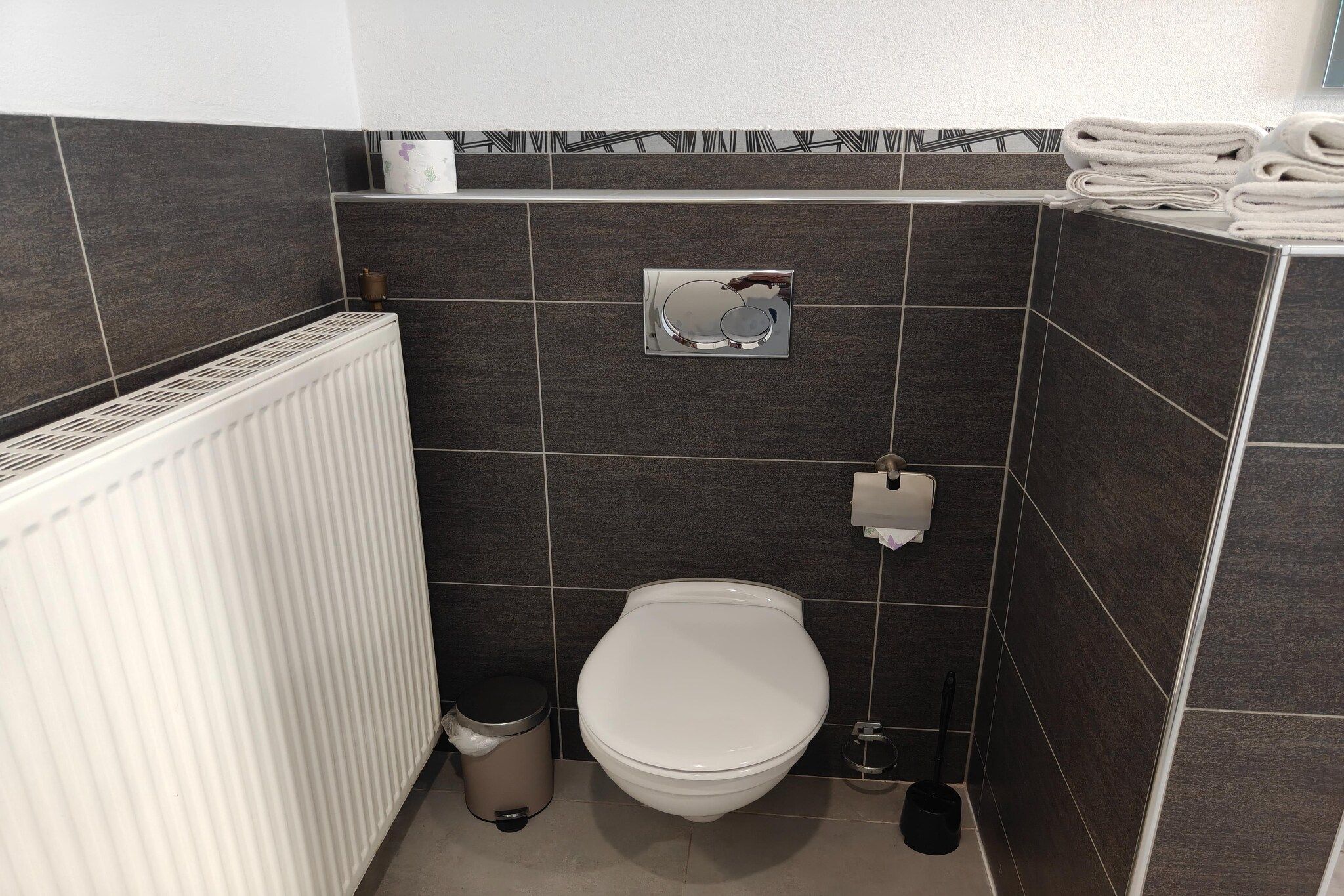 Ein kleines Badezimmer mit Toilette, Mülleimer, Heizkörper und Handtuchhalter.