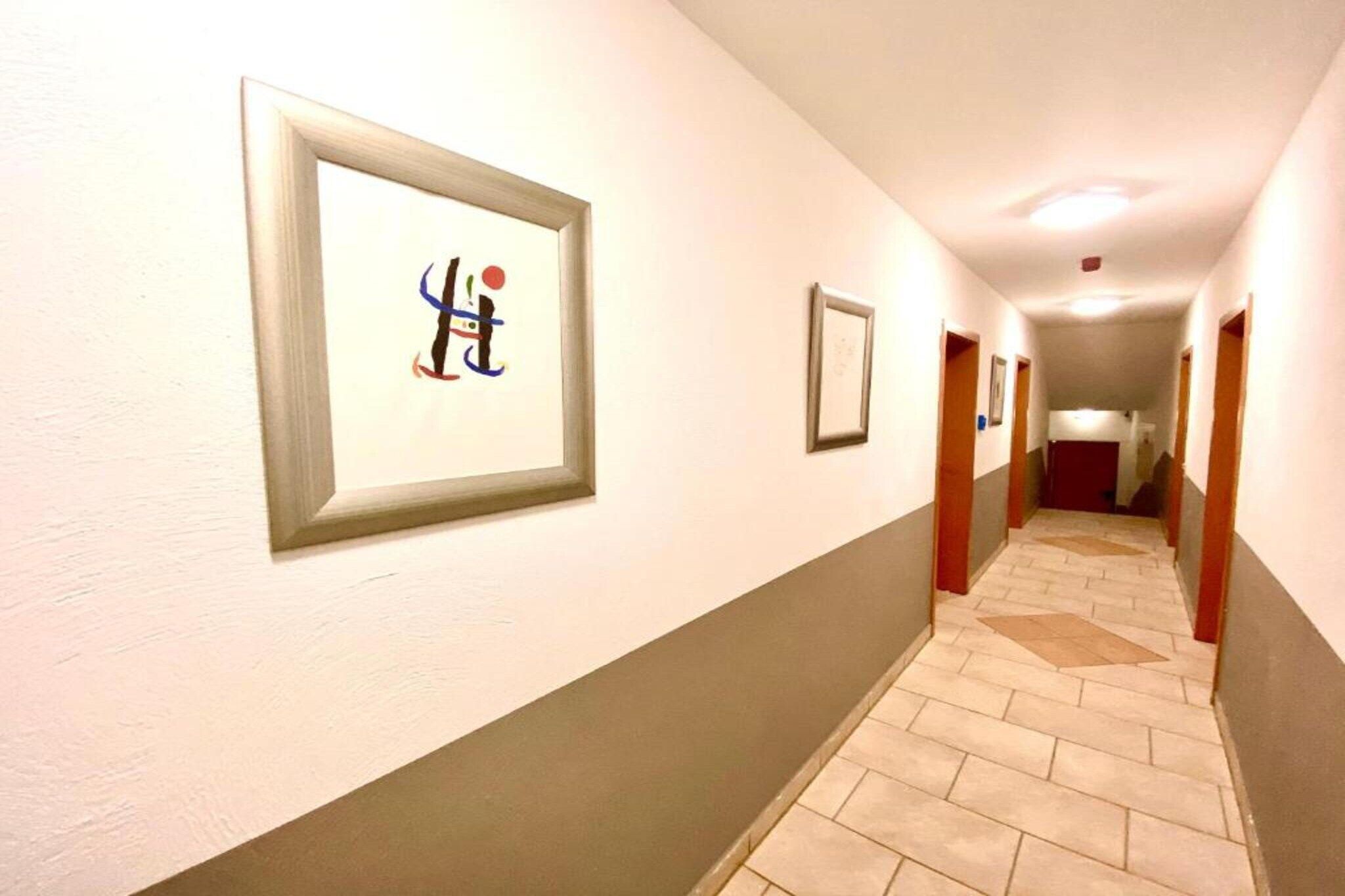 En hotelgang med indrammede kunstværker på væggene, et fliset gulv og døre til værelser.