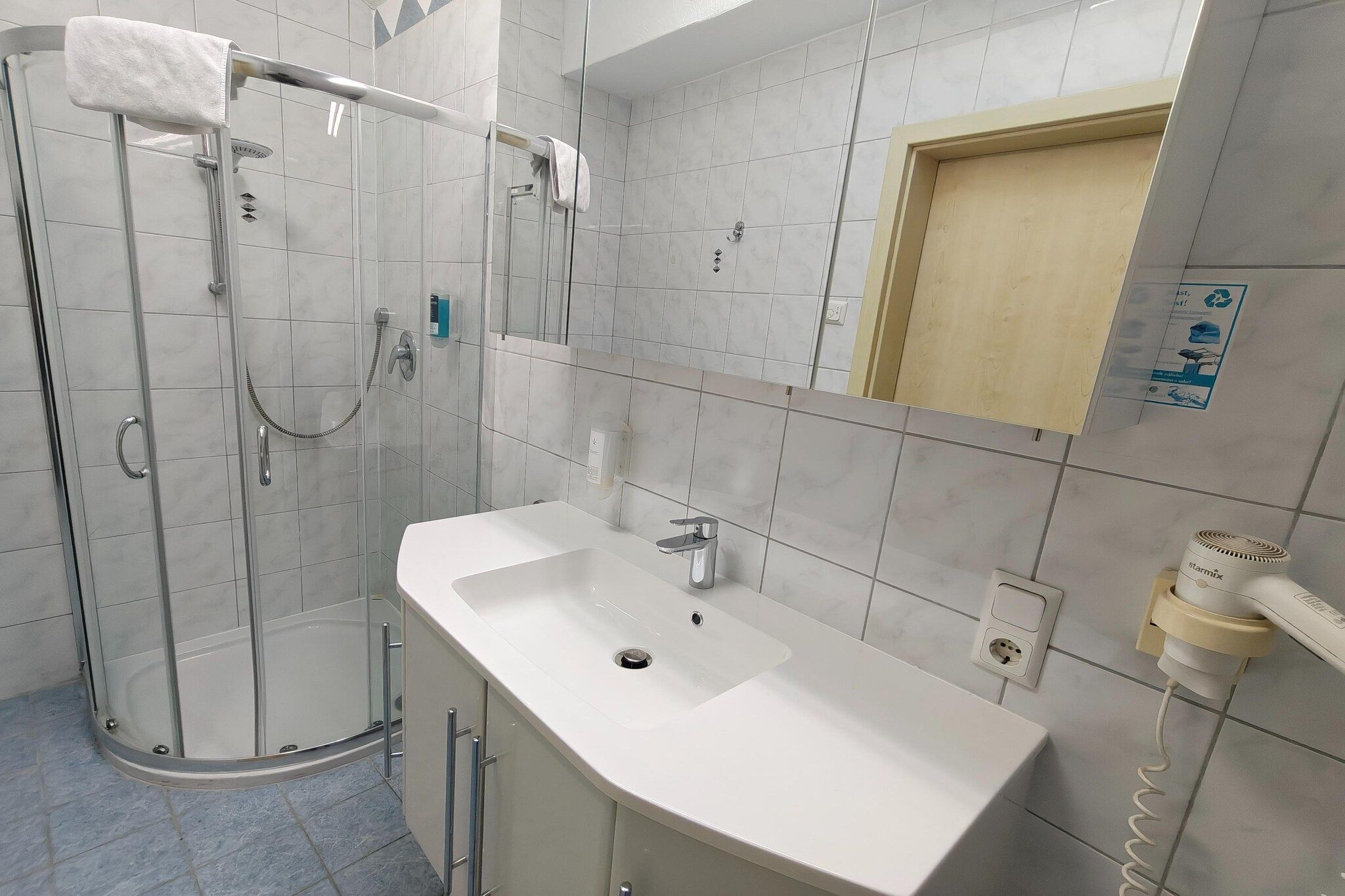 A modern bathroom with a glass-enclosed shower, a white sink, and a mirror.