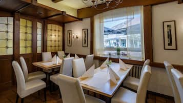 En restaurant med træpaneler, hvide stole og et stort vindue med udsigt til gaden.