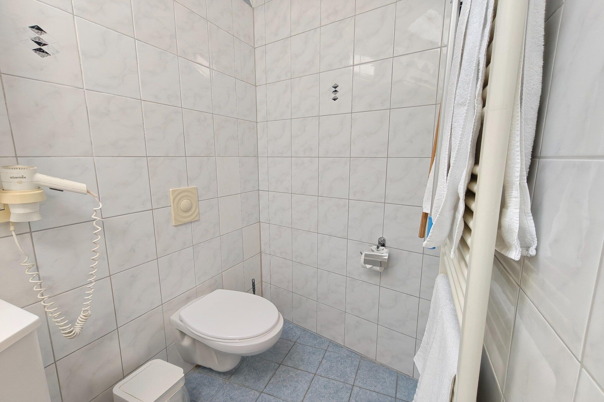 A small, tiled bathroom with a toilet, a hand dryer, and a towel rack.