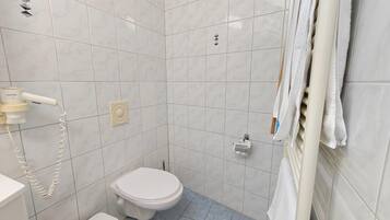 A small, tiled bathroom with a toilet, a hand dryer, and a towel rack.