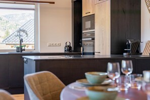 A modern kitchen with a central island, built-in appliances, and a dining area with a table set for two. - Chalet right next to the ski area (St. Lambrecht)