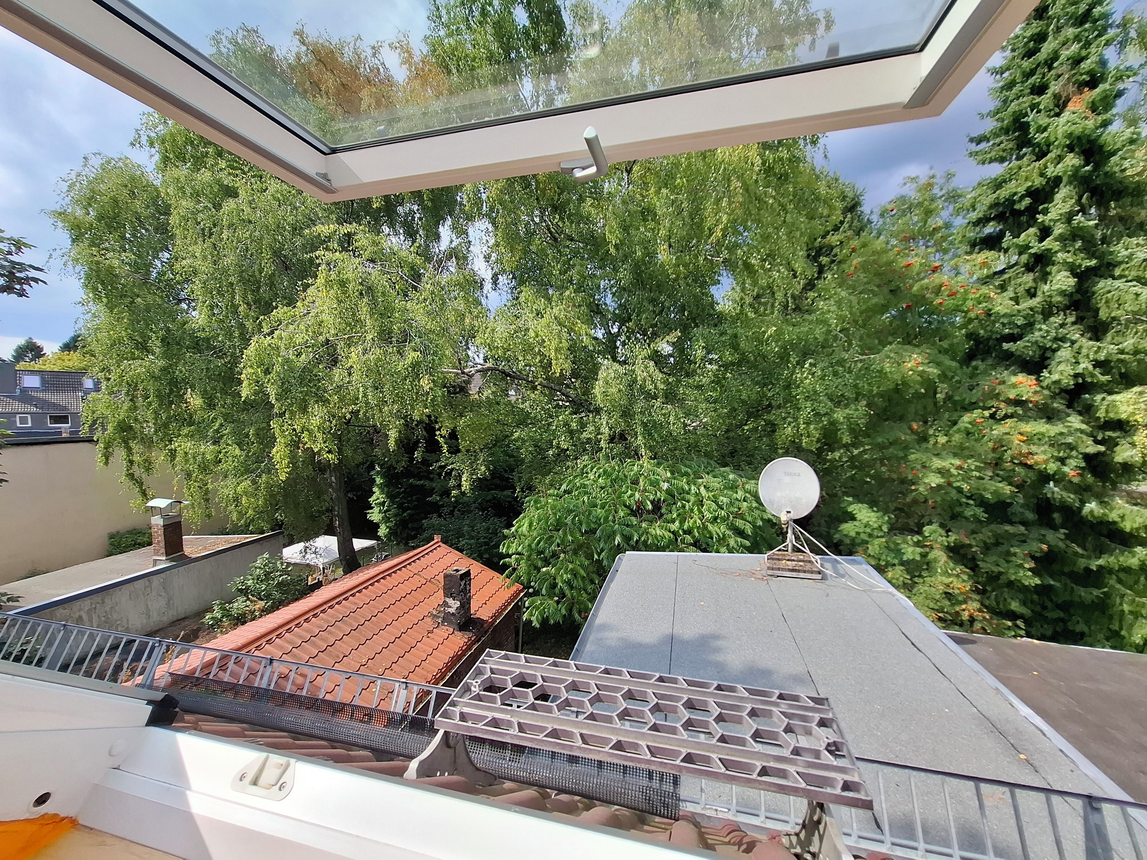 A room with a skylight, a satellite dish, and a view of trees and a building.
