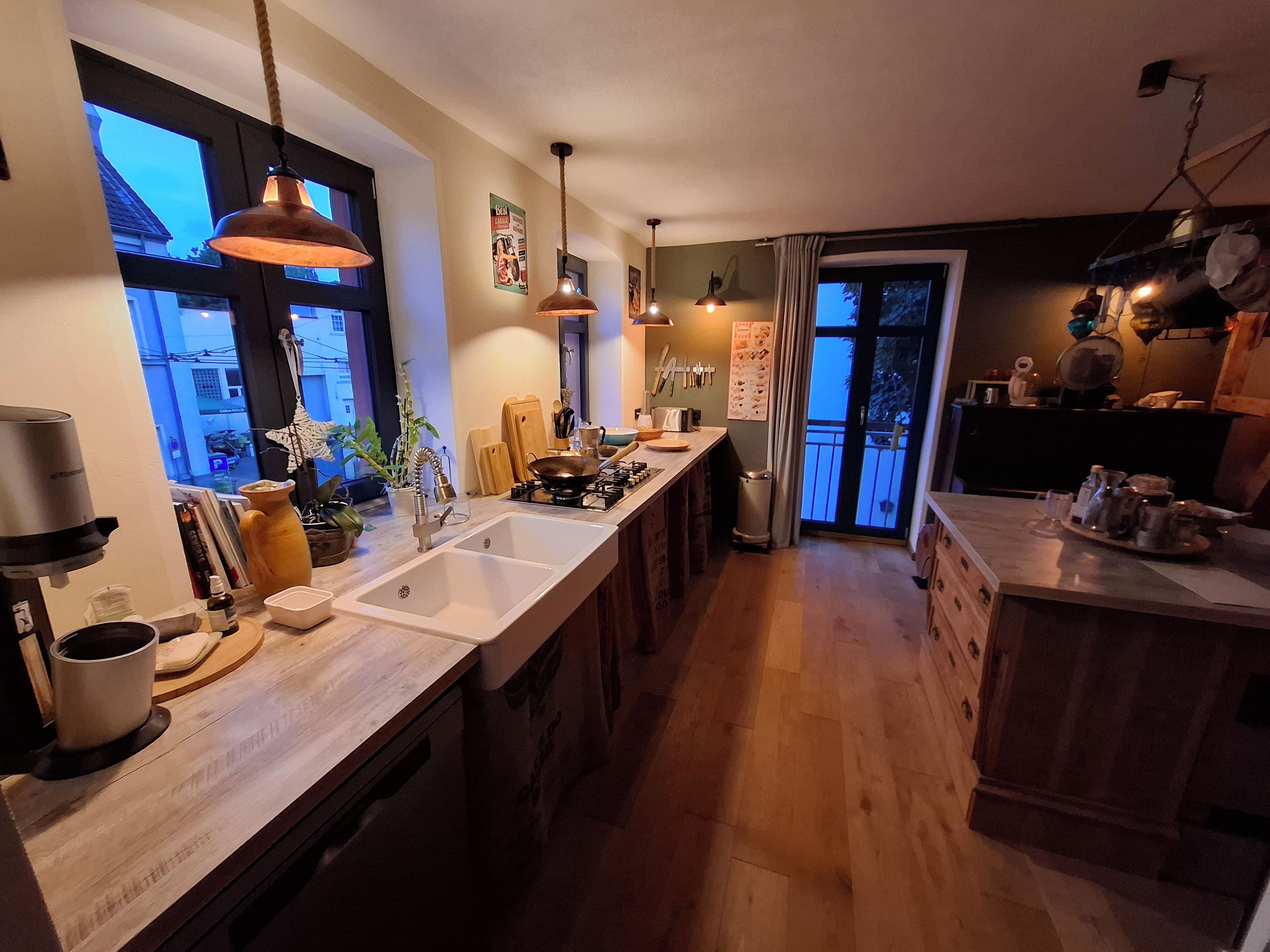 A kitchen with a long countertop, a sink, and hanging pendant lights.