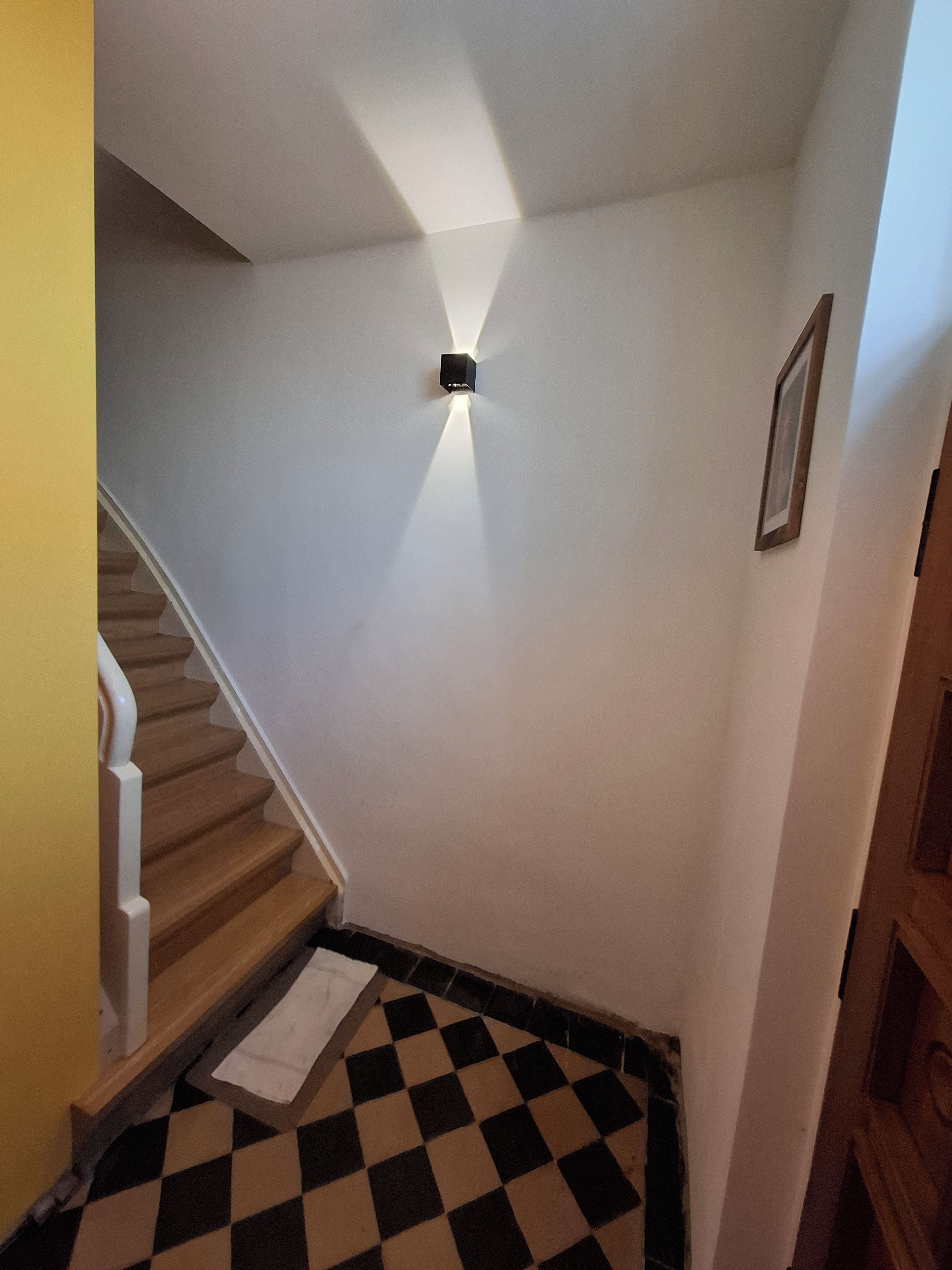 Eine Treppe mit Schachbrettmuster, einer weißen Wand und einer Leuchte.