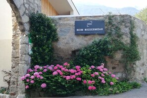 A stone wall with a sign that reads 'BEIM NIEDERMOR' and a cluster of pink flowers. - At Niedermoar- "Etschwool" (Naturns)