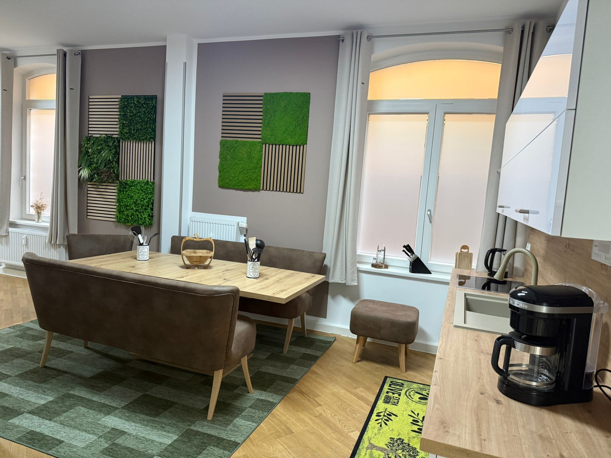 Un espace repas moderne avec une table en bois, des chaises à revêtement marron et un tapis à motifs verts.