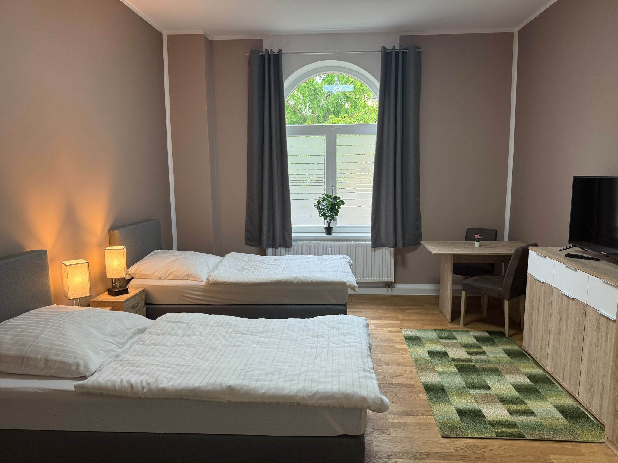 A hotel room with two beds, a desk, a television, and a window with curtains.