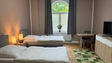 A hotel room with two beds, a desk, a television, and a window with curtains.