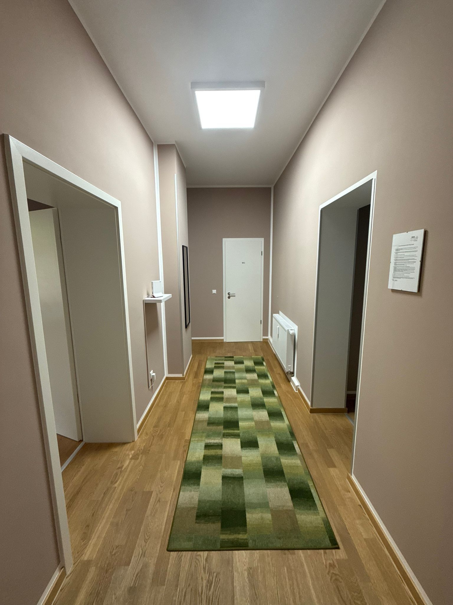 Um corredor com carpete quadriculado verde, piso de madeira e paredes brancas.