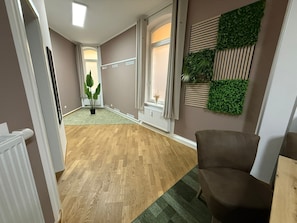 Un pasillo con suelo de madera, un radiador, una planta en maceta y un sillón marrón.
