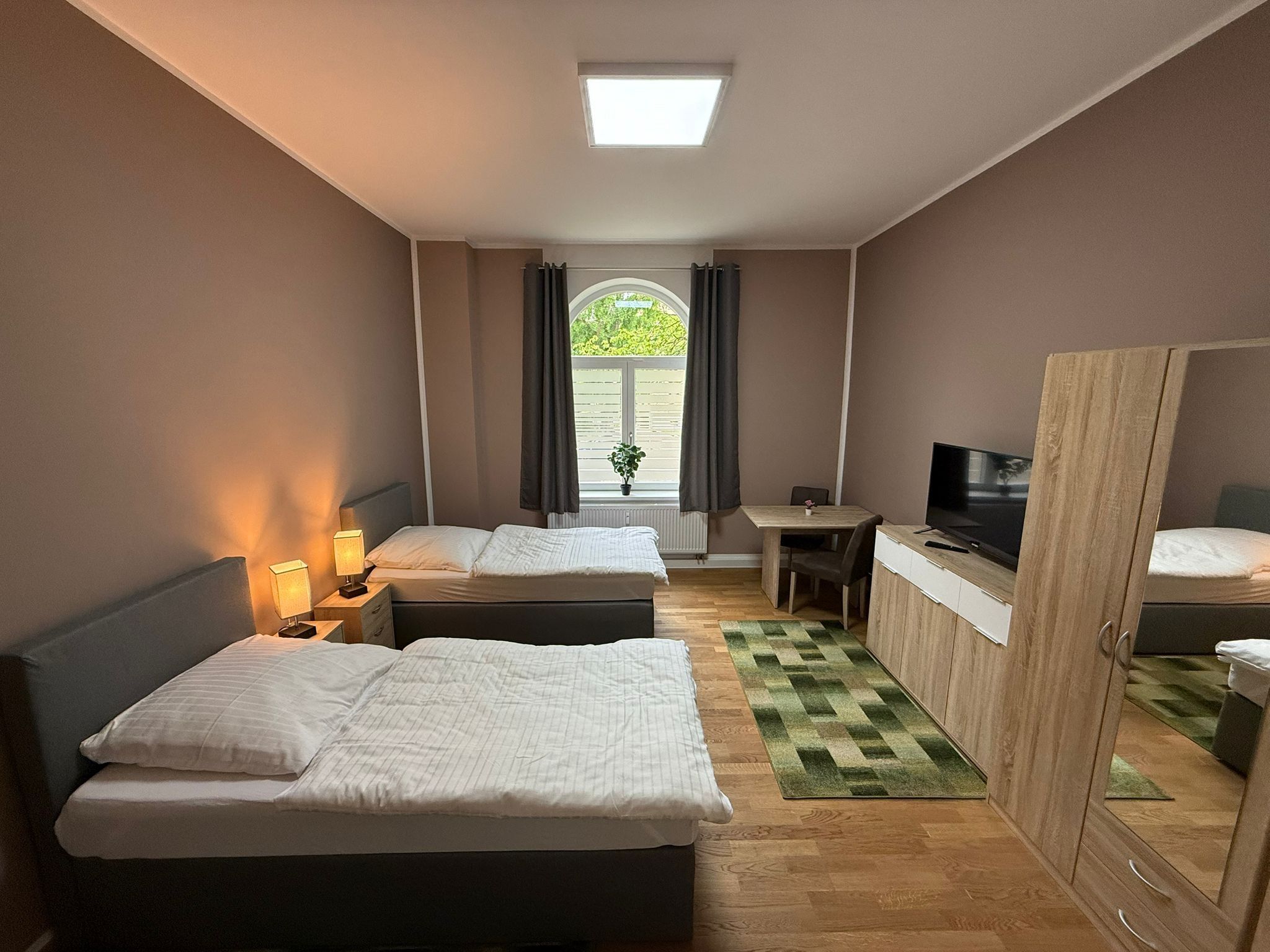Ein Hotelzimmer mit zwei Betten, einem Schreibtisch, einem Fernseher und einem Kleiderschrank.
