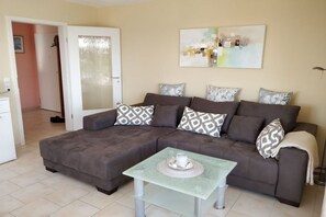 A living room with a sectional sofa, a small table, and a door leading to another room. - Holiday apartment with 2 bedrooms (Cuxhaven\/Sahlenburg)