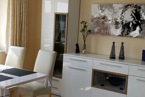 A modern dining area with a white table, chairs, and a glass partition. There is a painting on the wall and a vase with flowers on the table. - Holiday apartment with 2 bedrooms (Cuxhaven\/Sahlenburg)