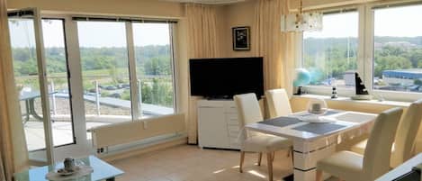 Una sala moderna con televisor de pantalla plana, comedor con mesa y sillas, y ventanas amplias que ofrecen vistas al exterior.