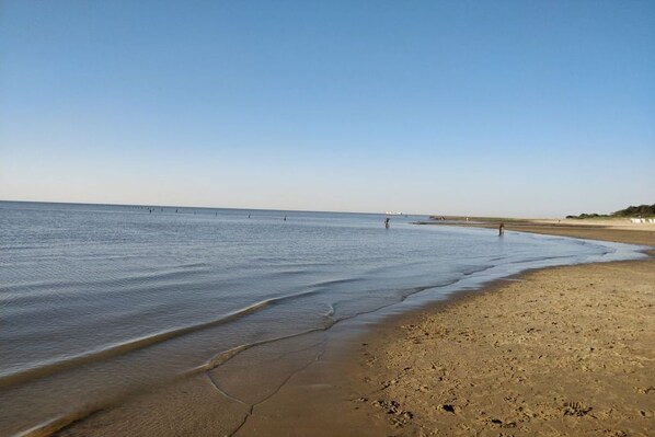 Ein Strand mit blauem Himmel, ruhigem Wasser und einigen Spaziergängern.