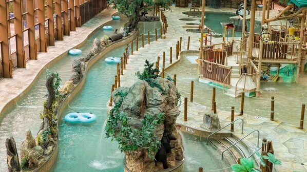 Um parque aquático em ambiente interno com diversas piscinas escorregadias, boias infláveis e uma estrutura de escalada em formato de urso.