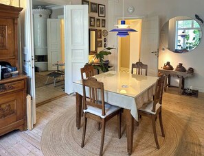 Ein Essbereich mit einem Glastisch, Holzsesseln, einer blauen Hängelampe und einem Spiegel an der Wand.