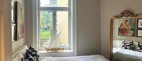 A bedroom with a large window, a bed with white bedding, and a small sailboat model.