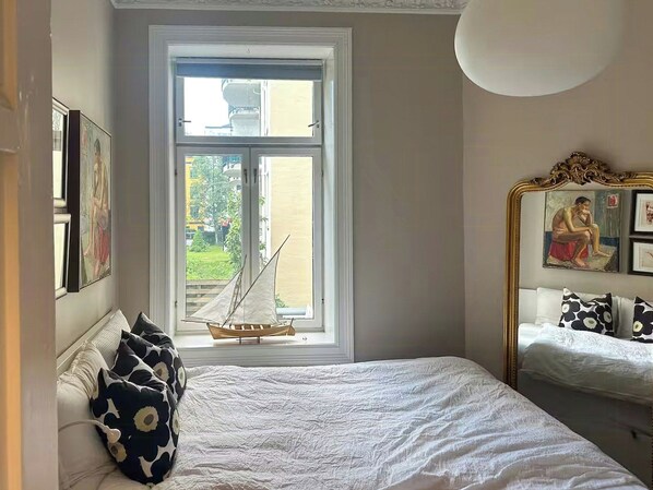 A bedroom with a large window, a bed with white bedding, and a small sailboat model. - Classic apartment in the heart of Majorstuen (Oslo)