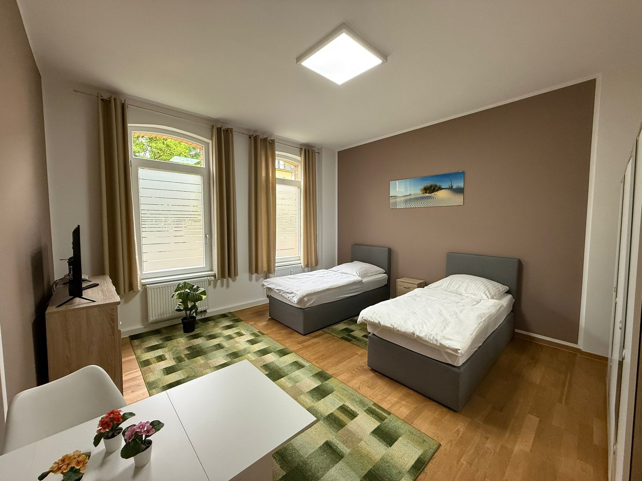 Un dormitorio con dos camas, un escritorio, una silla, un radiador y una ventana con cortinas.