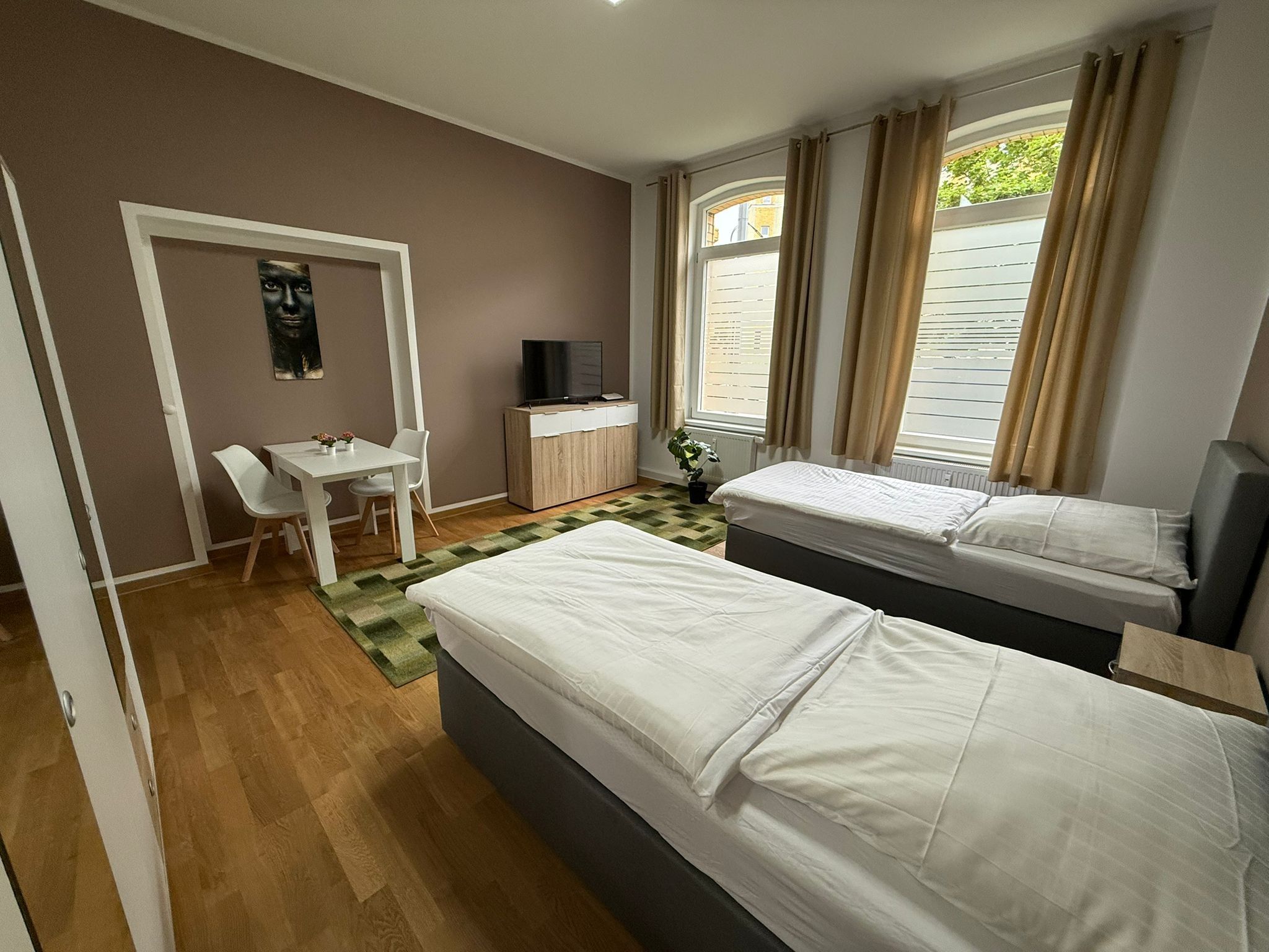 A hotel room with two beds, a desk, a TV, and a window with curtains.