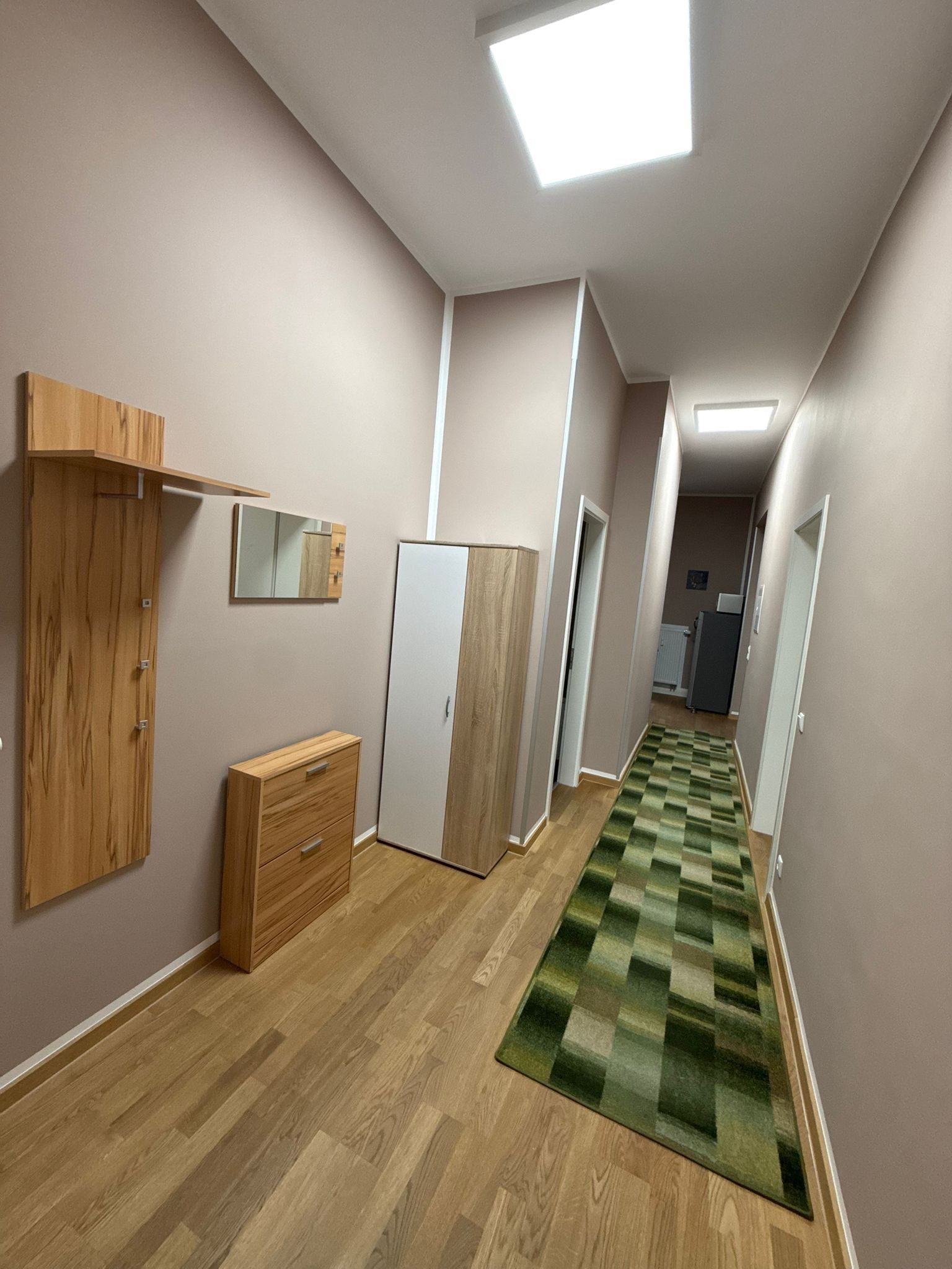 A hallway with wooden flooring, a green checkered carpet, and a white wardrobe.