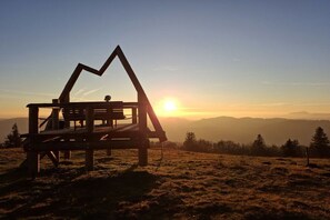 Un mirador de fusta amb estructura de teulat triangular, amb vistes a un paisatge muntanyós durant el capvespre.