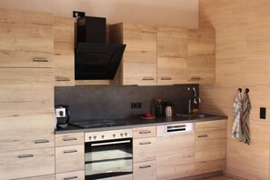 A modern kitchen with wooden cabinetry, a built-in oven, a coffee maker, and a kettle on the countertop. - Holiday apartment Bernau Dorf (Bernau)