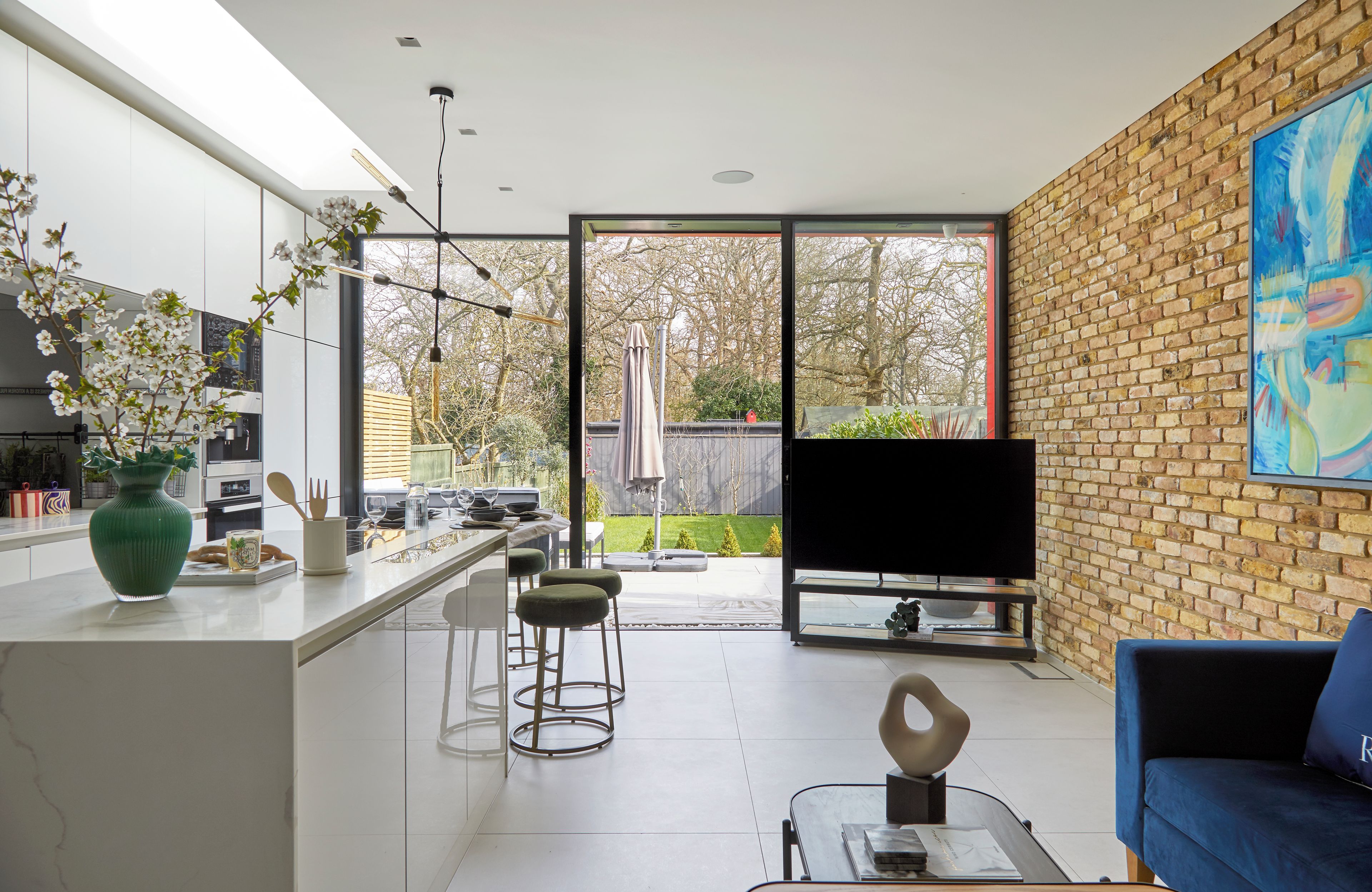 A modern kitchen with a large island, bar stools, and a dining area with a TV and sofa.