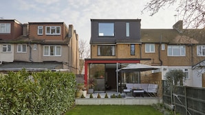 Een wooneenheid met een moderne patio, een constructie met rode kozijnen en een verzorgde tuin.