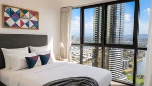 Habitación de hotel con una cama grande, vistas a un paisaje urbano y una obra de arte geométrica en la pared.
