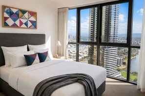 Ein Hotelzimmer mit einem großen Bett, Blick auf eine Stadtansicht und einem geometrischen Kunstwerk an der Wand.
