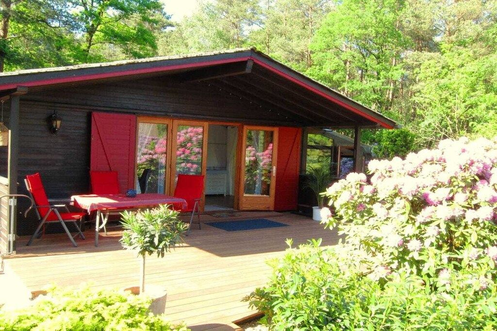 A wooden cabin with a covered deck, red chairs, and a small table.
