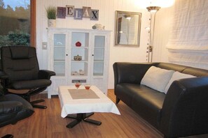 Ein Zimmer mit einem schwarzen Ledersofa, einem schwarzen Sessel, einem kleinen Tisch mit weißer Tischdecke und einer Vitrine mit Glastüren.
